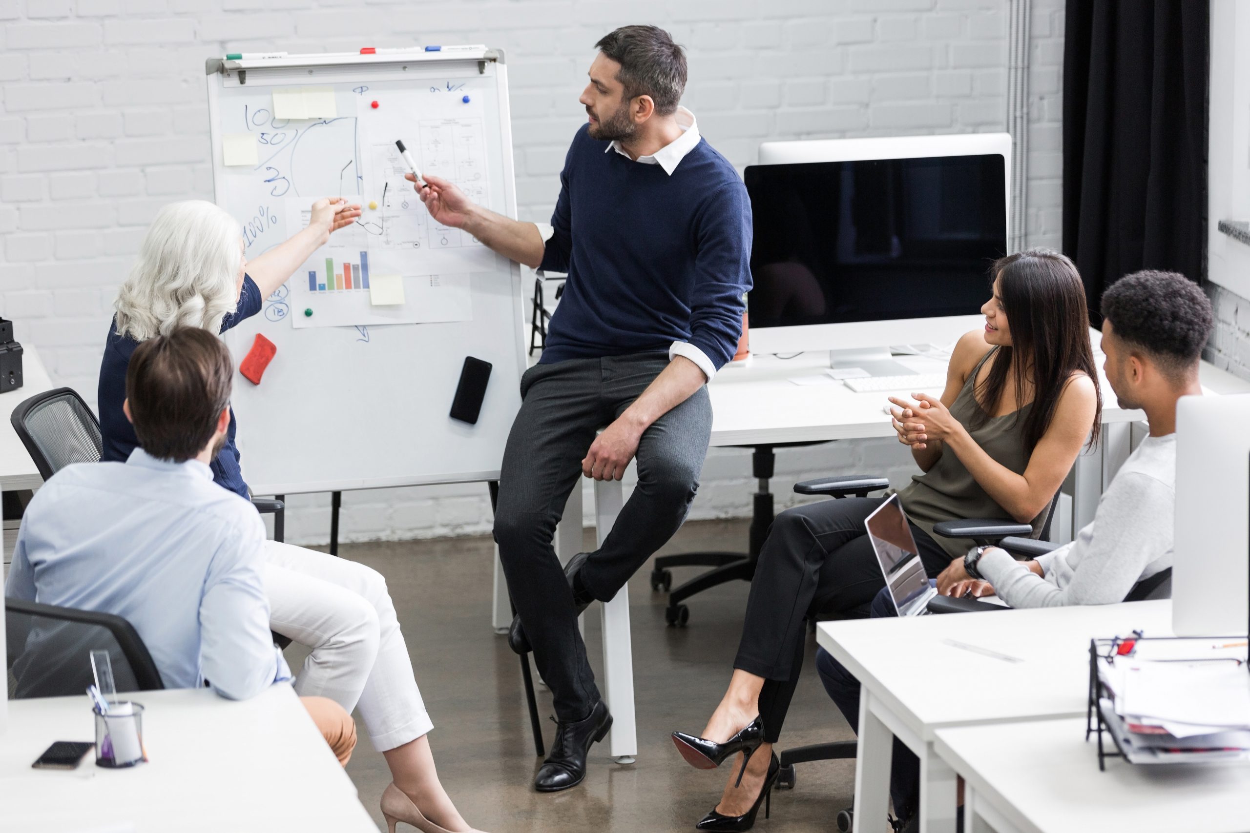 Creative people sitting at table in boardroom with man explaining business strategy
